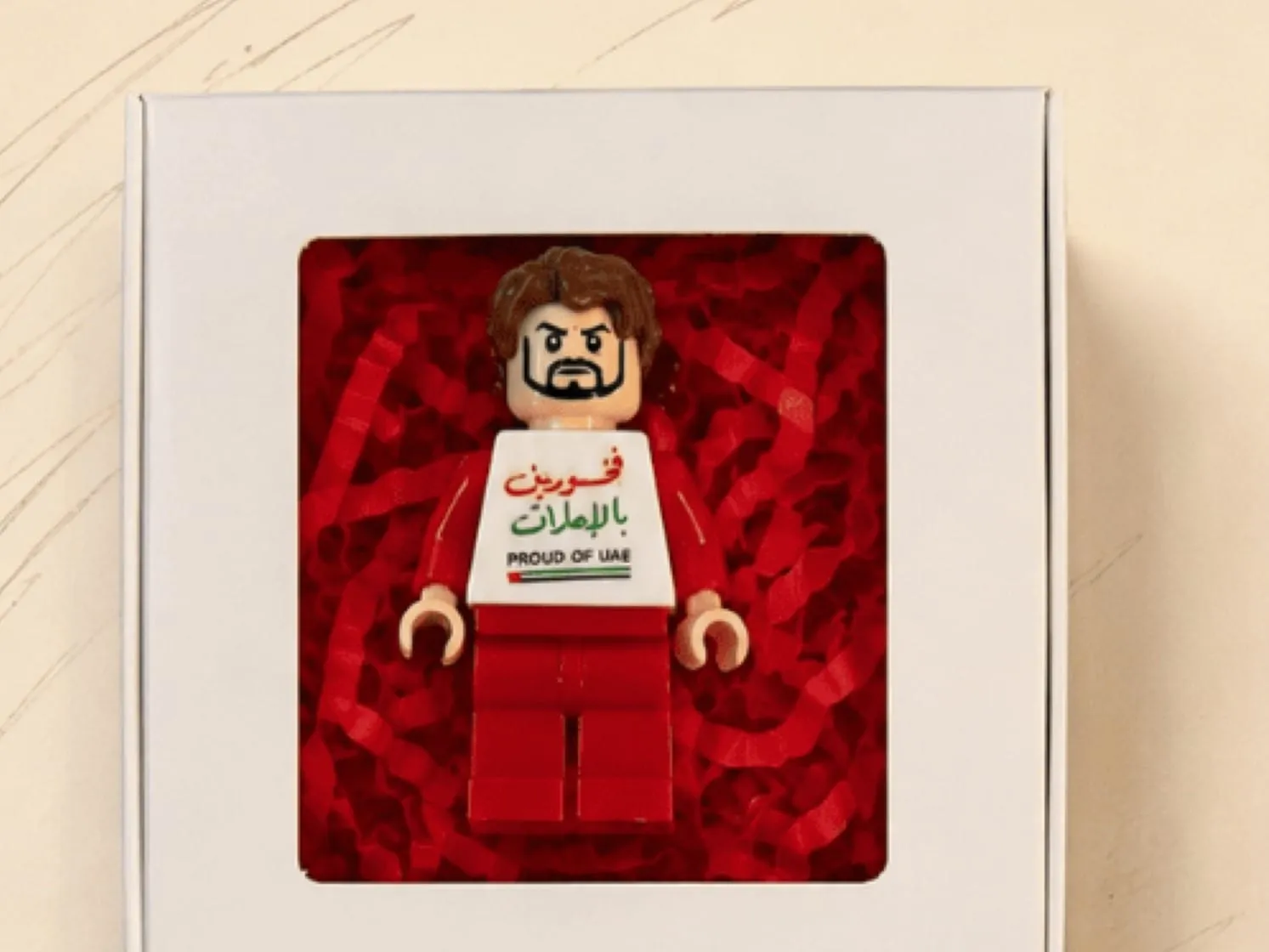 A mini figure in red wearing a Proud of UAE torso, packed in a gift box with a window